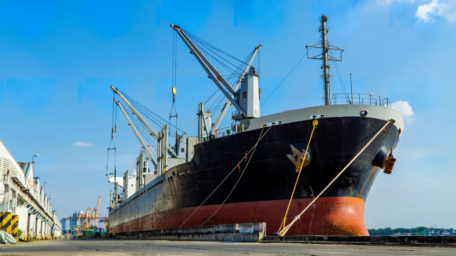 General cargo vessel alongside a port berth with ship's cranes.